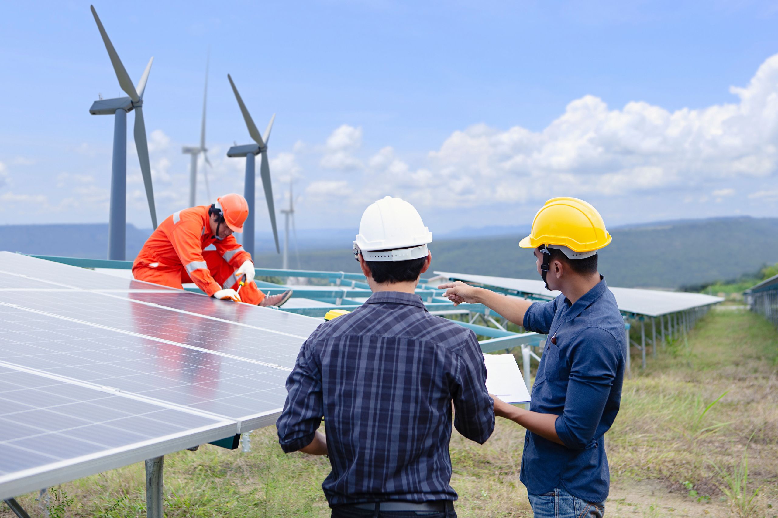 Three workers standing by a wind power grid.